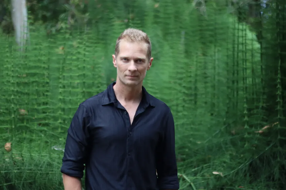Josh Galt with arms crossed in front of a wall of horsetail ferns