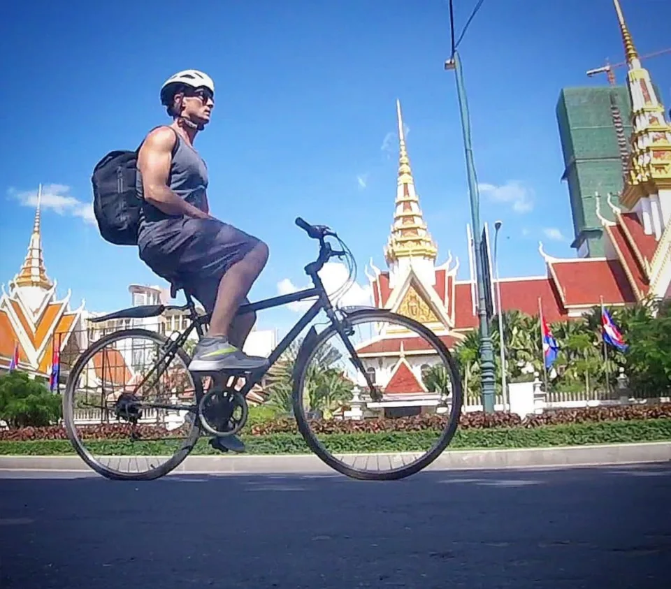 Josh Galt on a bicycle in front of a golden-roofed pagoda in Phnom Penh