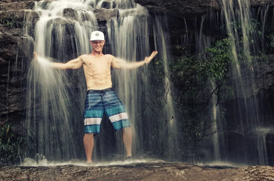 Josh Galt standing under a curtain waterfall in Cambodia, arms out
