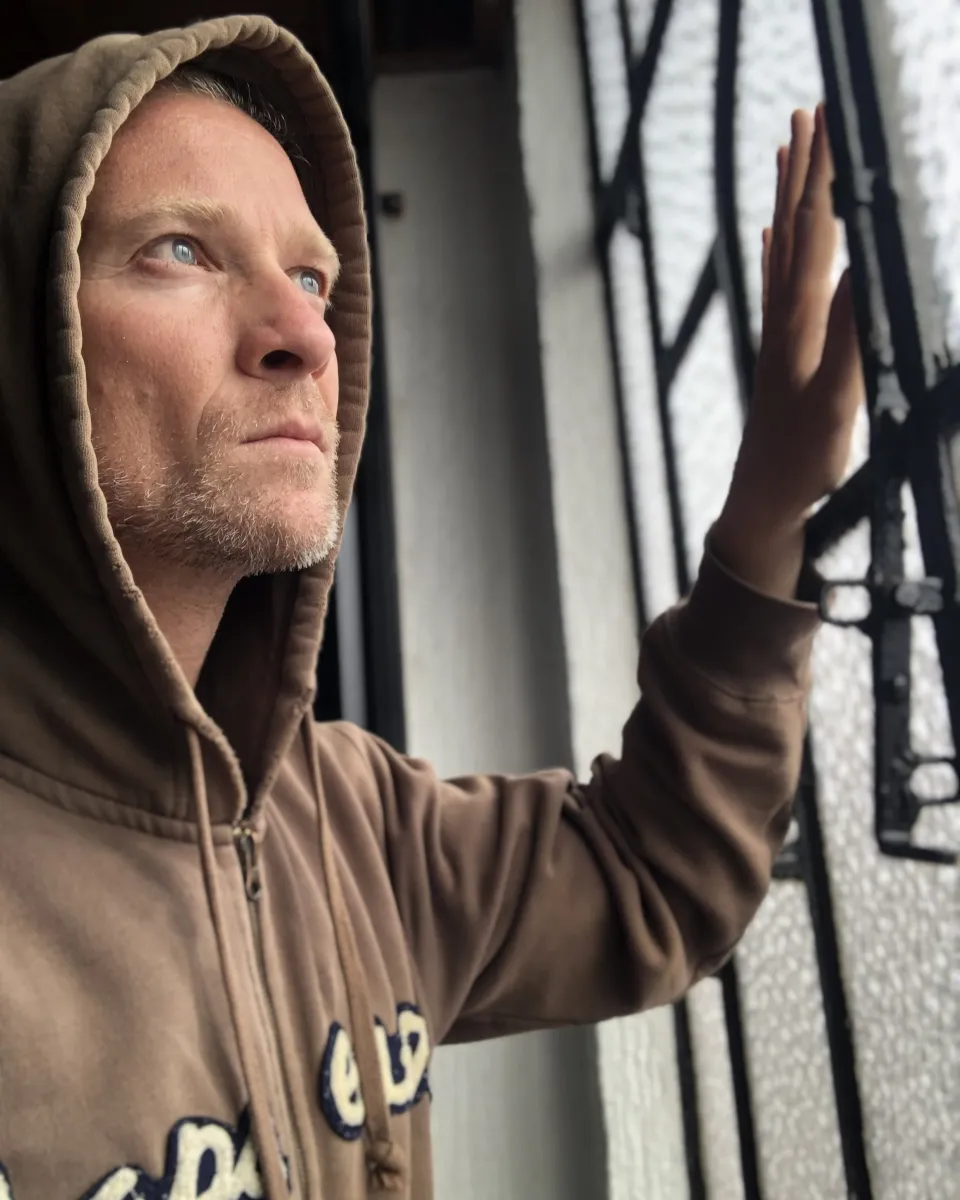 Josh Galt in a hooded sweatshirt, hand on a barred window, looking out